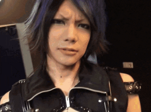 a woman with purple hair is making a face and wearing a black vest