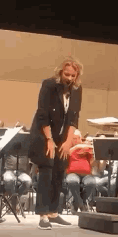 a woman is standing on a stage in front of an orchestra while a child sits in the audience .