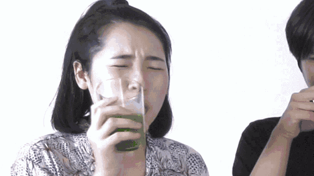 a woman drinking a glass of green juice