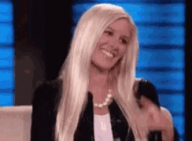 a woman with long blonde hair is sitting on a couch smiling .
