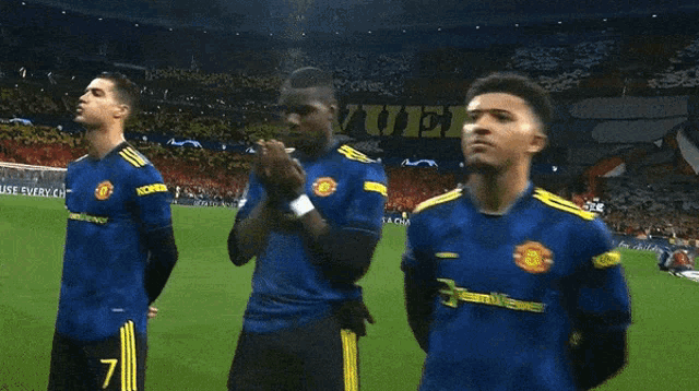 a soccer player wearing a blue jersey with yellow stripes on the sleeves prays on the field