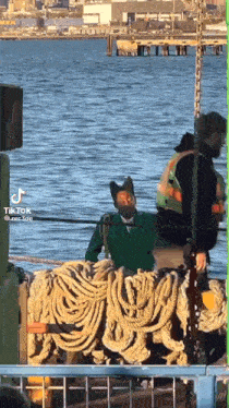 a man in a green jacket is sitting on a boat with ropes around it