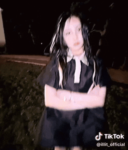 a girl in a black dress is standing with her arms crossed and a tiktok watermark at the bottom