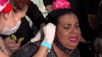 a woman is getting her ear pierced by a nurse while wearing a pink hat .