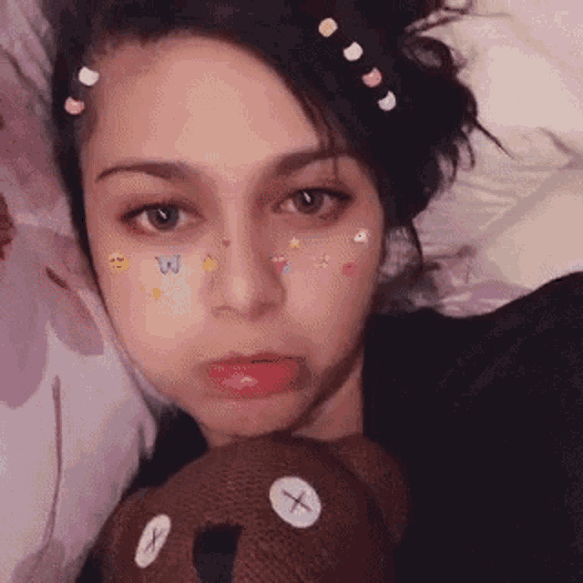 a woman is laying on a bed with a teddy bear and stickers on her face .