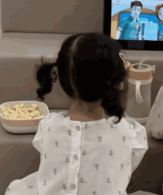 a little girl is sitting at a table watching a tv