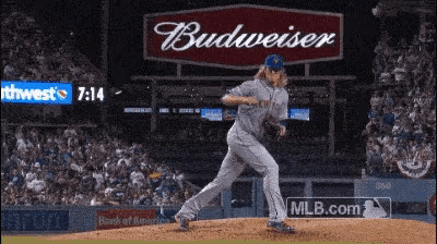 a baseball pitcher winds up to throw the ball with a budweiser sign in the background