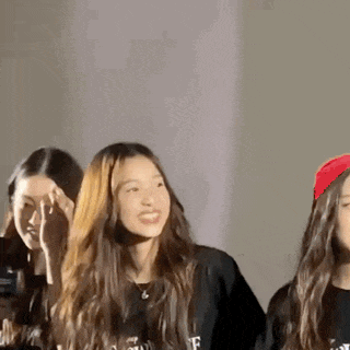 three young women are standing next to each other in a room . one of the girls is wearing a red hat .