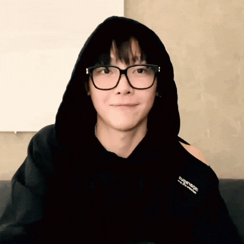 a young man wearing glasses and a black hoodie is smiling for the camera .