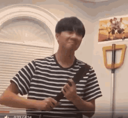 a young man in a striped shirt is holding a guitar in his hands .