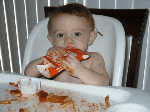 a baby sitting in a high chair eating a bag of tortilla chips