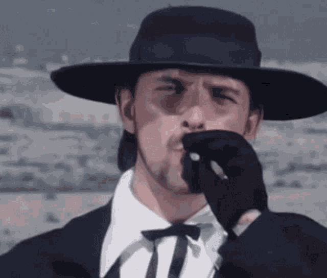 a man in a hat and gloves smoking a cigarette