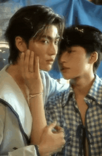 a couple of young men are standing next to each other and one of them is touching the other 's face .