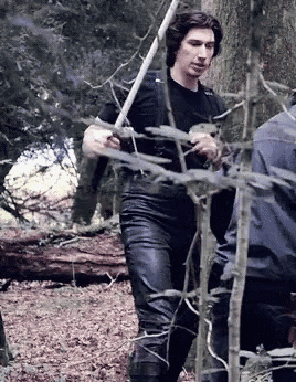 a man in a black shirt is walking through a forest holding a stick .