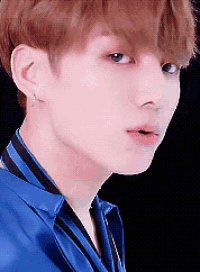 a close up of a young man 's face wearing a blue shirt and earrings .