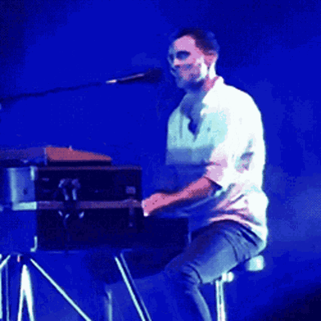a man in a white shirt is playing a keyboard on stage