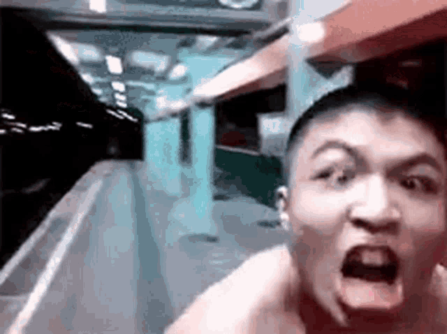 a man without a shirt is standing in front of a train with his mouth wide open .
