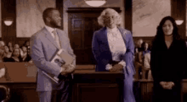 a man in a suit and tie is standing in a courtroom next to a woman in a purple suit .