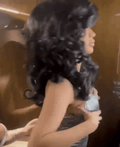 a woman in a wig is standing in a room holding a cell phone .