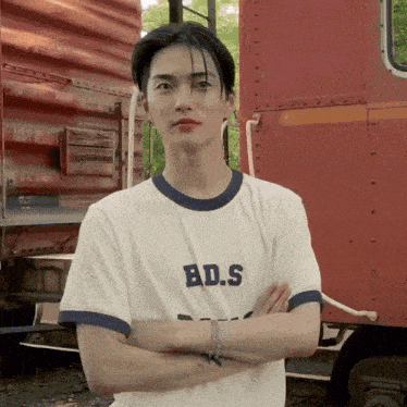 a young man with his arms crossed wearing a bd.s shirt