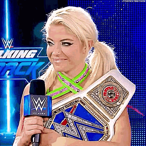 a woman is holding a microphone and wearing a wrestling championship belt .
