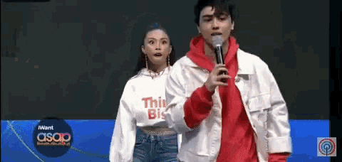 a man in a red hoodie is holding a microphone next to a woman in a white sweatshirt that says this big