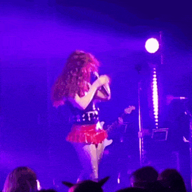 a woman in a red skirt is singing into a microphone on stage