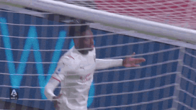 a soccer player in a white jersey is pointing at the goal net .