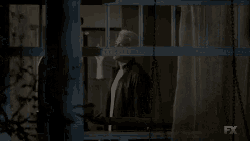 a man is standing in front of a window with a curtain behind him .