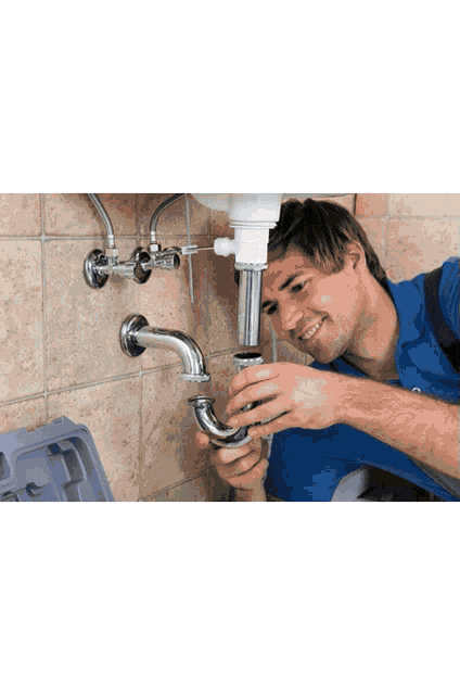 a man in a blue shirt is fixing a pipe under a sink
