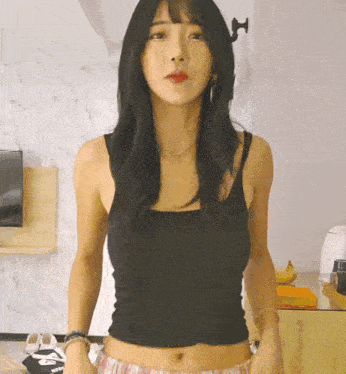 a woman in a black tank top is standing in front of a wall