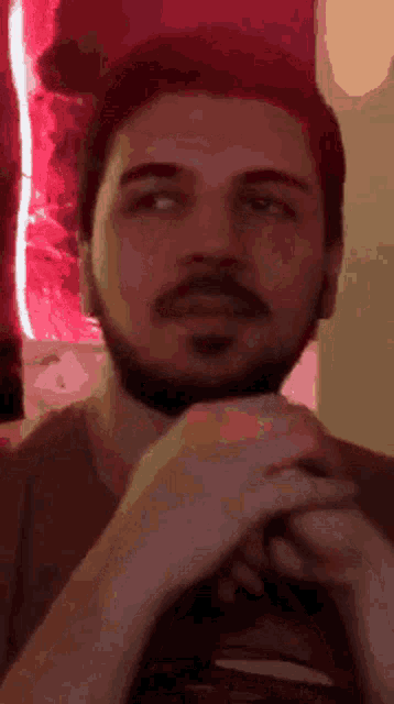 a man with a beard is looking at the camera with his hands folded in front of him .