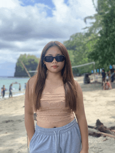 a woman wearing sunglasses and a crop top stands on the beach