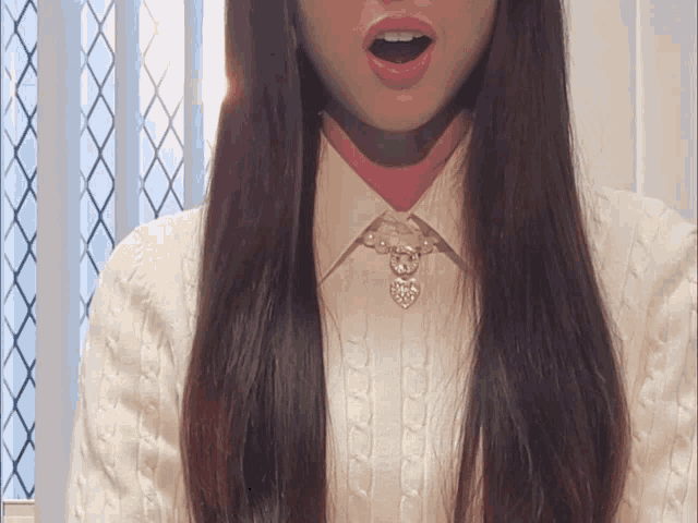 a woman with long hair wearing a white sweater and necklace
