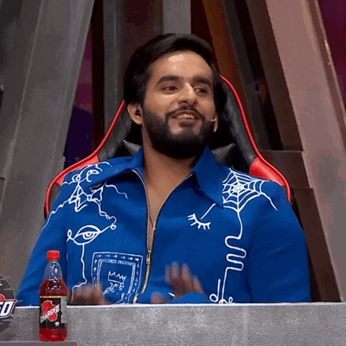 a man in a blue jacket is sitting in a chair next to a bottle of powerade