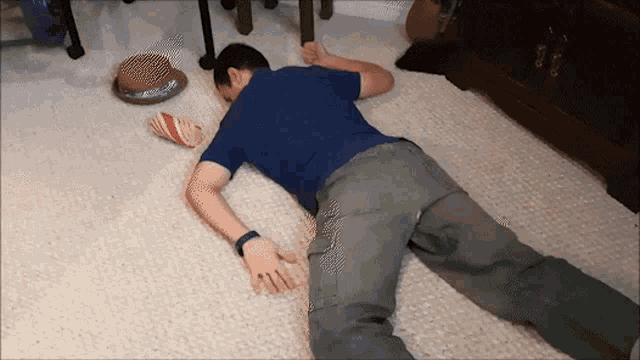 a man in a blue shirt is laying on the floor next to a cat bowl
