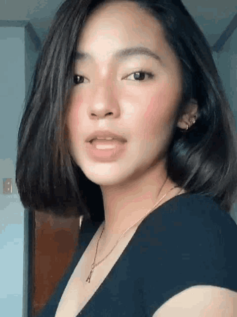 a woman with short hair is wearing a black shirt and a necklace and looking at the camera .
