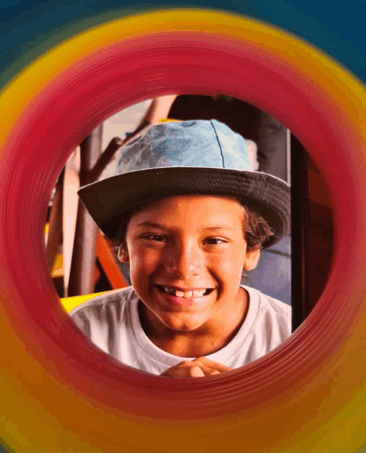 a young boy wearing a hat is smiling through a rainbow colored tunnel