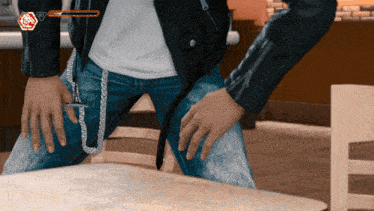 a man in a leather jacket is sitting at a table with his hands on his knees