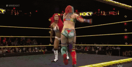 two women are wrestling in a ring while a crowd watches .