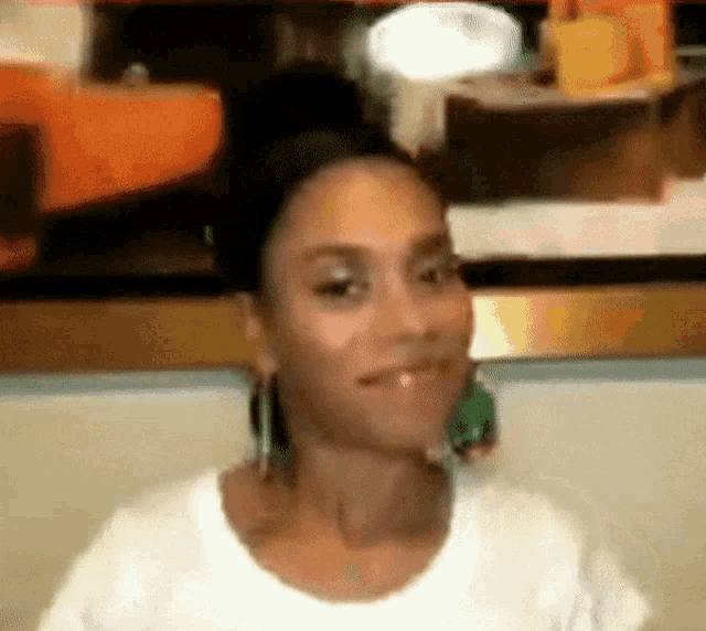 a woman wearing a white shirt and green earrings is smiling and looking at the camera .