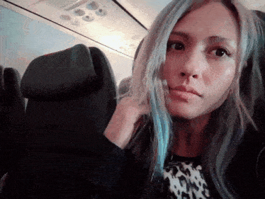 a woman with blue hair is sitting in a plane seat