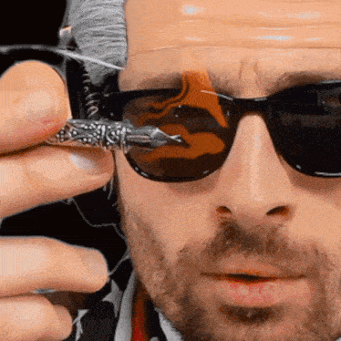 a man wearing sunglasses holds a pen in front of his eye
