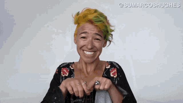 a woman with yellow and green hair is smiling and making a funny face .