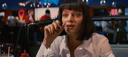 a woman smoking a cigarette in a diner with a red bottle of ketchup on the table