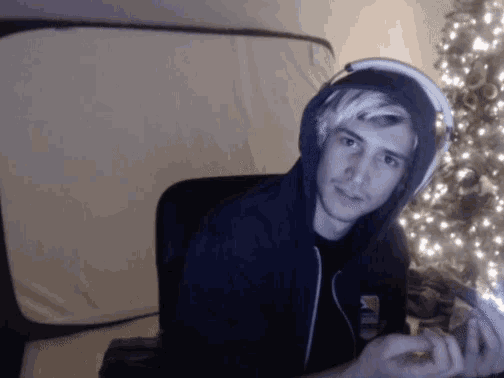a young man wearing headphones and a hoodie looks at the camera