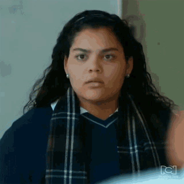 a young woman in a school uniform is wearing a scarf and making a funny face .