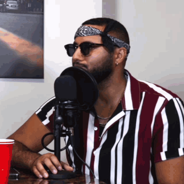 a man wearing sunglasses and a bandana sitting in front of a microphone