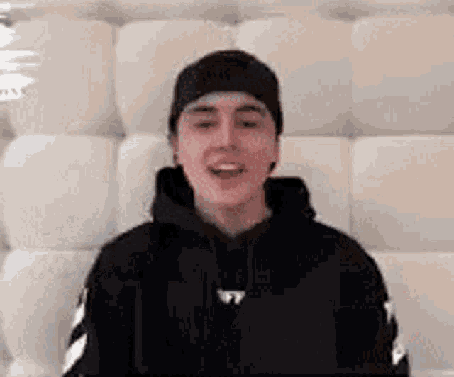 a young man wearing a black hoodie and a hat is sitting on a white couch .
