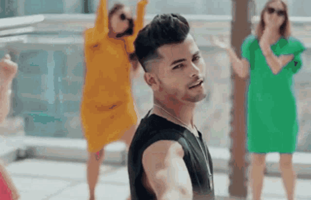 a man in a black tank top is standing in front of two women dancing .